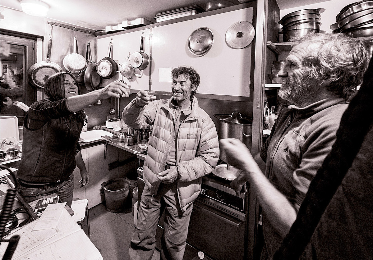 Inside the kitchen of the Promontoire Refuge, built in 1901 by the Club Alpin Francais (and rebuilt in 1966) at 3092 meters, guardians Nathalie Clerc and Fredi Meignan enjoy a glass of genepi with La Grave guide Pierre Cinquin. The summer of 2018 was Meignan’s last after a decade as a guardian. He recalls the season as unusually warm. [Photo] Abdou Martin