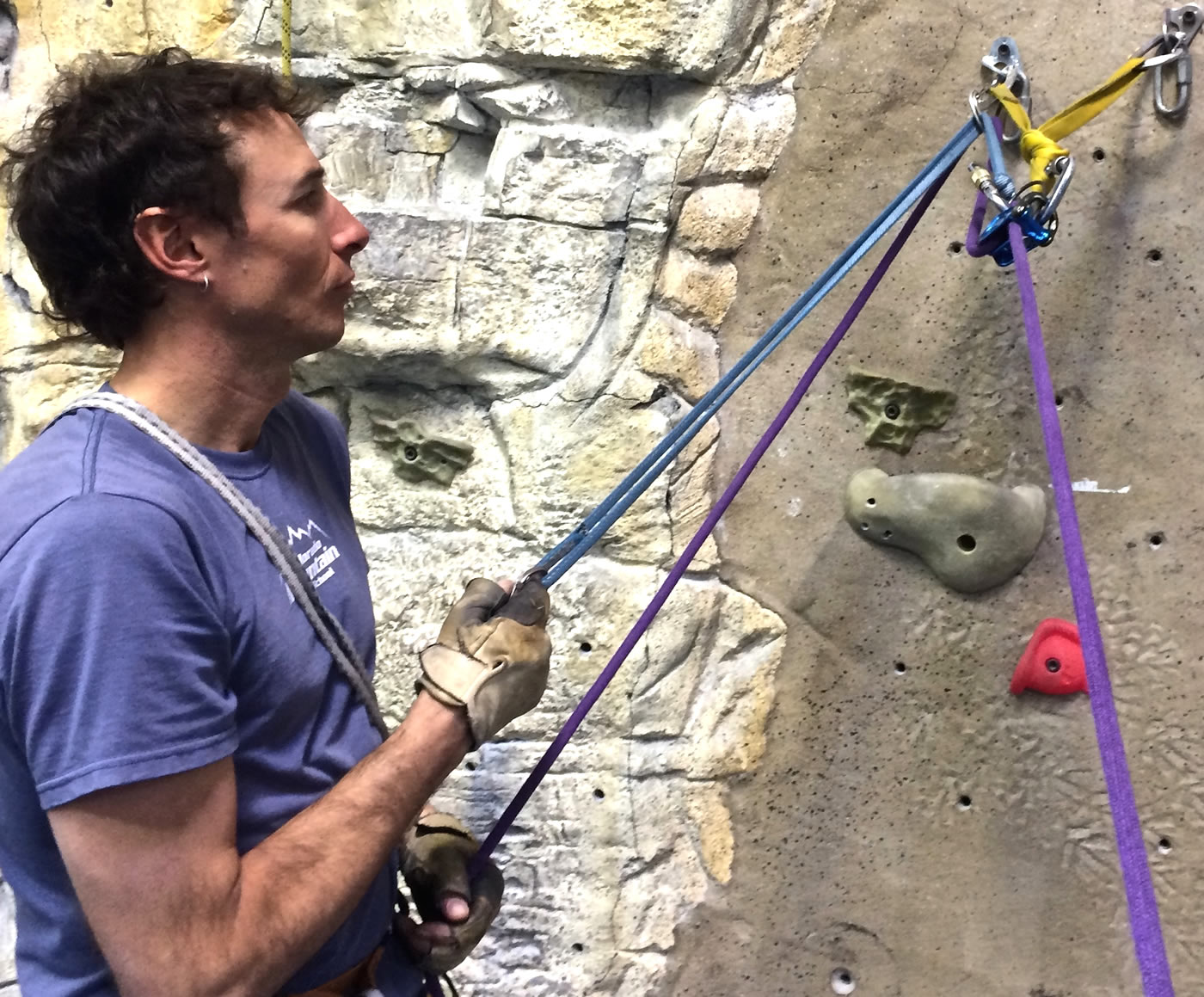 Mike Lewis demonstrates how to lower a climber while in guide mode with the DMM Pivot: The belayer can set up a sling to pull back the carabiner on the rope and release the friction on the brake-end of the rope, allowing it to slide through the device while maintaining control with the brake hand. It may be necessary to use a backup on the brake-side of the rope to ensure control.