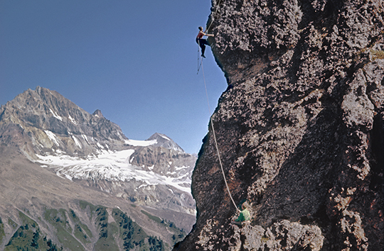 Fred Beckey, belayed by Les McDonald, climbs in British Columbia. Mt Garibaldi (2678m) is in the background, August 10, 1958. [Photo] Ed Cooper